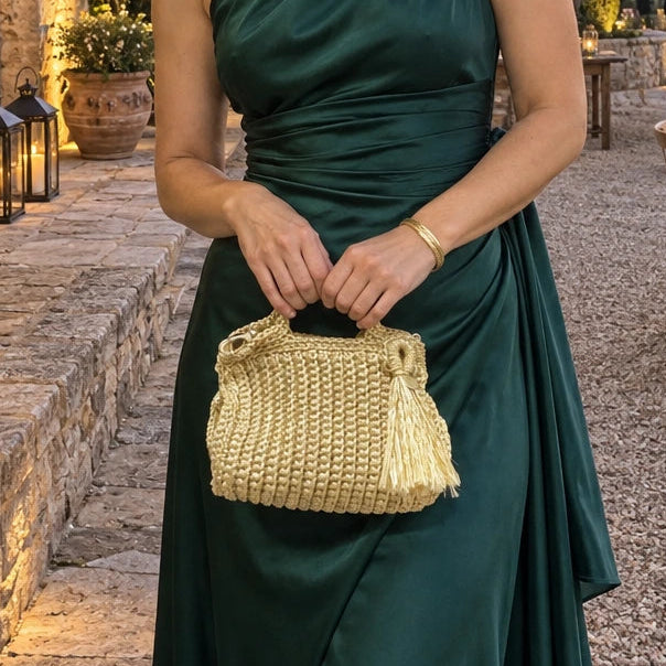 Bolso de Mano Nador Metalizado | A raw and authentic lifestyle photograph of a 30-year-old European woman, wearing a premium emerald green guest dress.