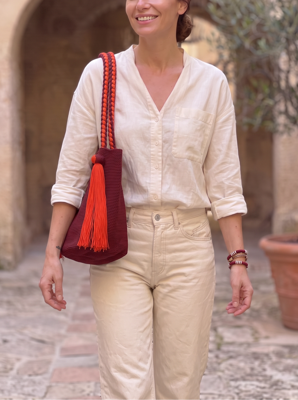 Bolso Wayúu LamuJoyas tejido a mano en algodón color burdeos con asas trenzadas y borla decorativa naranja.