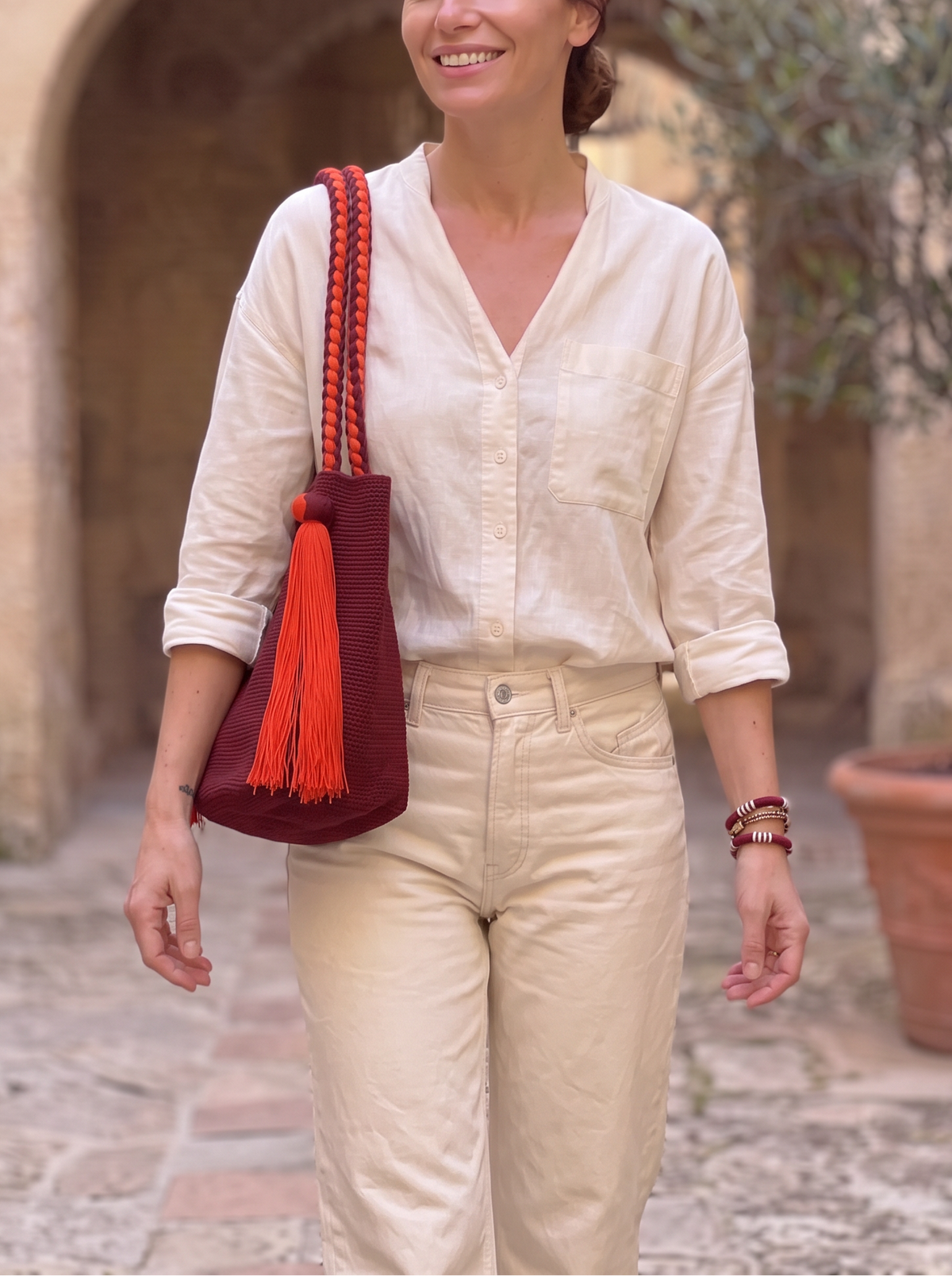 Bolso Wayúu LamuJoyas tejido a mano en algodón color burdeos con asas trenzadas y borla decorativa naranja.