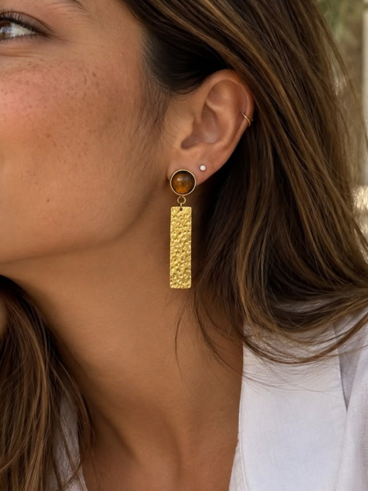 Pendientes Omari de LamuJoyas con pieza de latón martillado y detalle circular en tono ámbar, hechos a mano.