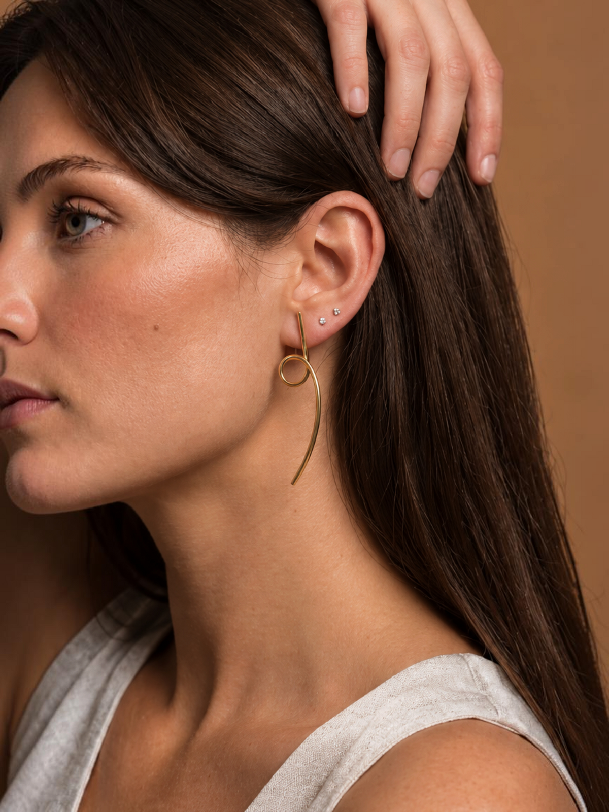 Pendientes Saba de LamuJoyas en latón dorado con diseño artesanal curvo, lucidos por una modelo de perfil.
