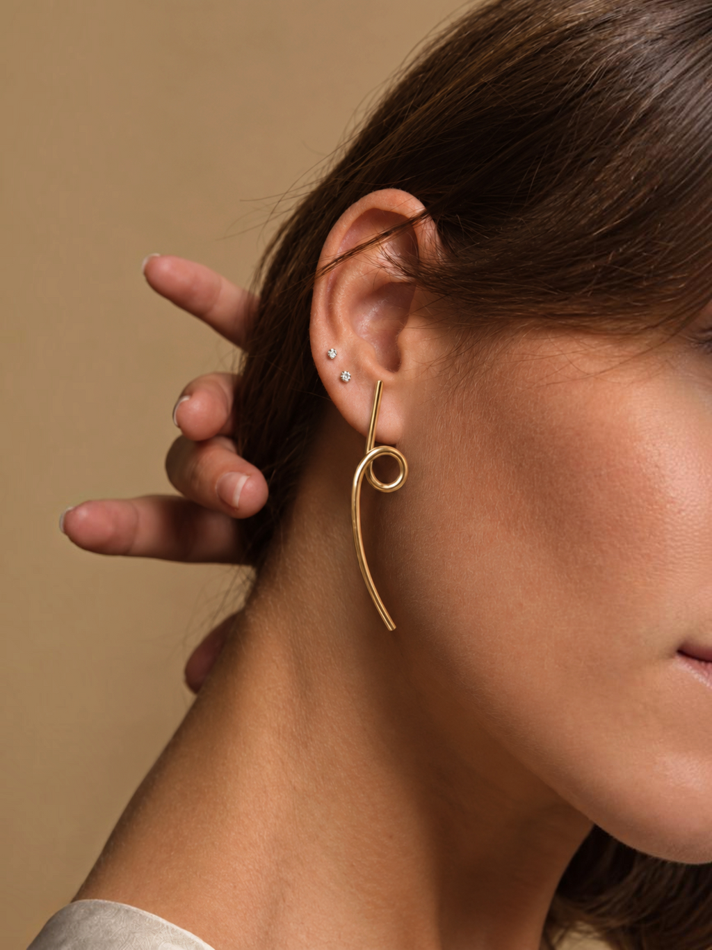 Pendientes Saba de LamuJoyas en latón dorado con diseño artesanal curvo y minimalista puestos en una oreja